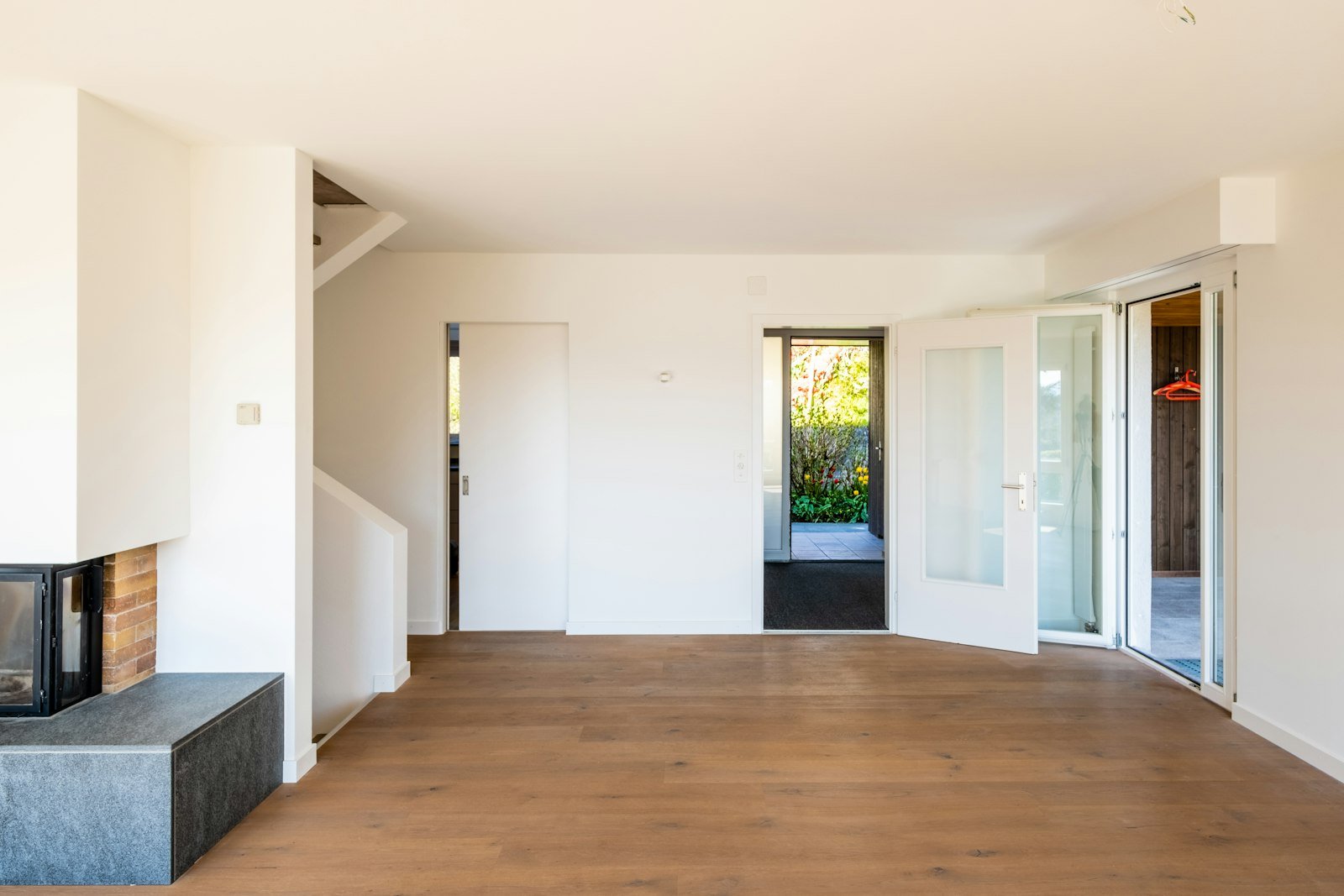 Leerer heller Wohnraum mit Eichenparkett, Kaminofen auf Granitsockel und Terrassentür zum Garten — besenrein übergebene Immobilie vor der Vermarktung